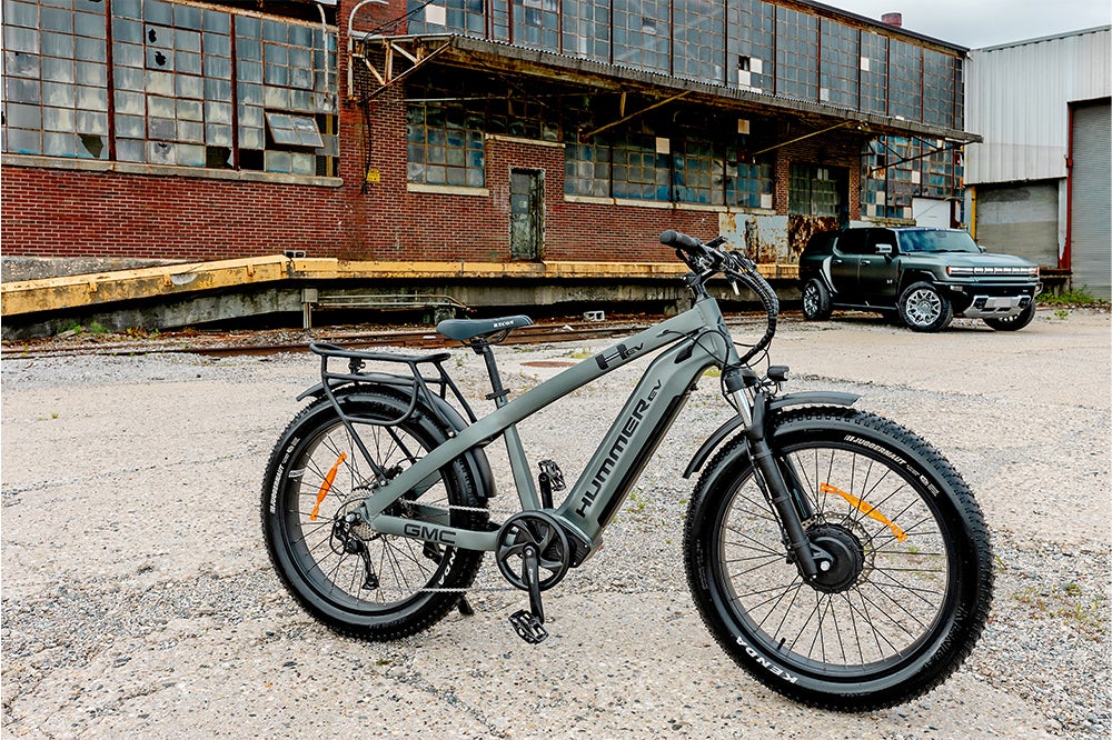 The AWD Electric Bike and Hummer EV are parked in front of a worn, old building.